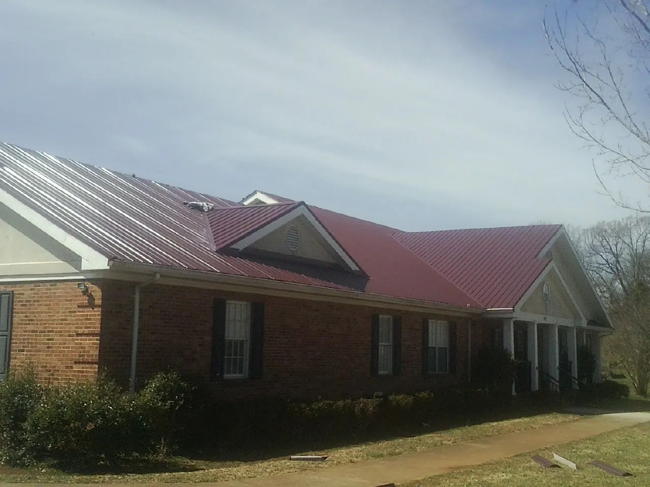 Red metal roof with gabled entries on a long brick building, from a Hail Damage Roof Repair job in Rockwall