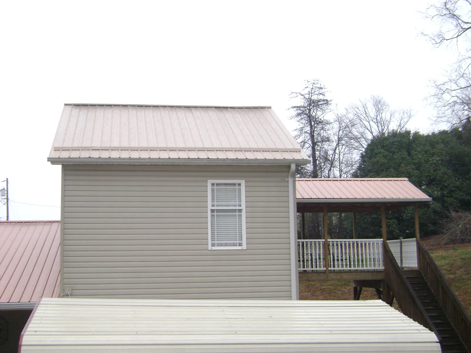 Tan metal roofs on a two story addition and attached porch, from a Roof Replacement job in Rockwall